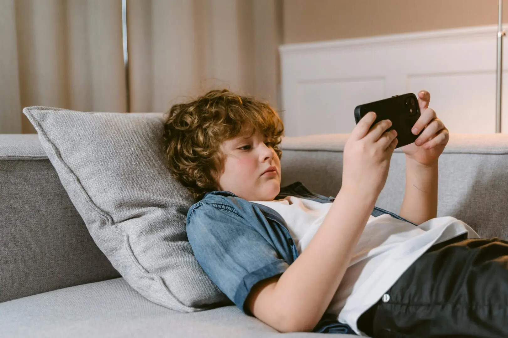 A boy is laying on the couch looking at his phone.